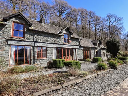 Stone house with wooden framed windows and gravel walkway surrounded by shrubs and trees at The Stables in Ambleside