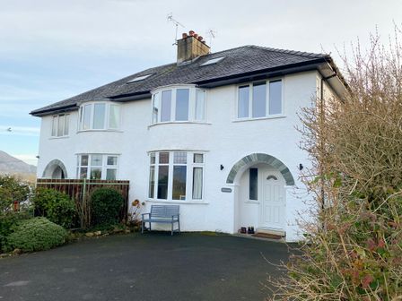 White two-story house with arched entrance door driveway and garden at Riggside in Portinscale