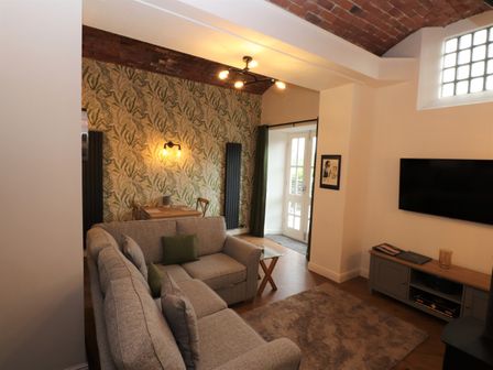 A living room with a gray sofa a small dining table with chairs patterned wallpaper and a wall-mounted tv at Fair Cop in Hawkshead