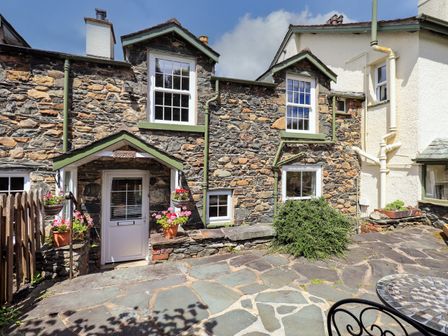 Stone cottage with white door surrounded by flower pots and a paved patio at Sandburne Cottage in Keswick