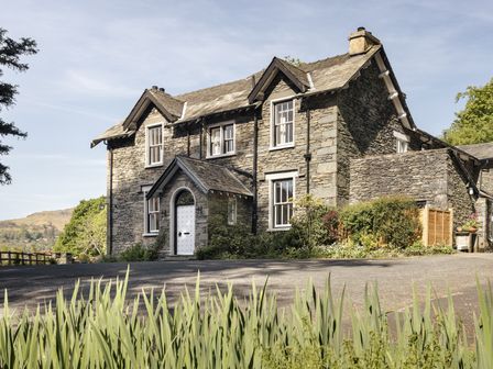 A stone house with white framed windows and a white door surrounded by plants and trees at Wetherlam in Grasmere