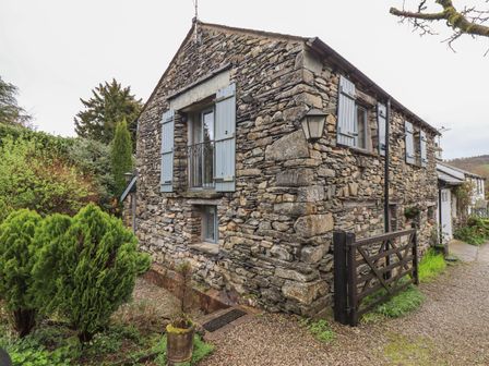 A stone house with blue shuttered windows a wooden gate and green bushes at Hannakin Barn in Hawkshead