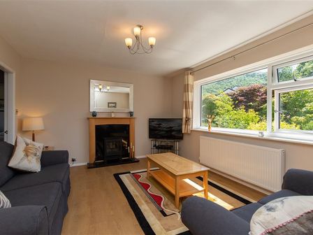 A living room with two sofas a wooden coffee table fireplace and a large window showing trees at Greenways in Ambleside