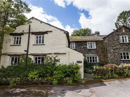 An exterior view of a stone and white plaster house with multiple windows surrounded by plants at High Fold in Troutbeck