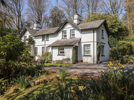 A white two story house with chimneys surrounded by trees and flowers at Hodge How Cottage in Windermere