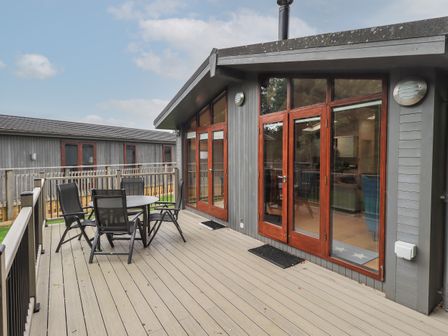 An outdoor deck with a round table and four chairs outside a house with wooden double doors at Beck of Beyond in Ambleside