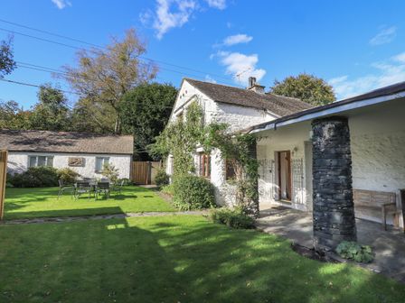 A yard with green grass tables and chairs a white stone house with a covered porch and stone pillar at Croft in Grasmere