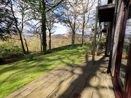 A patio with stone paving next to a grassy area and trees near a house at Puddleduck in Skelwith Bridge near Chapel Stile