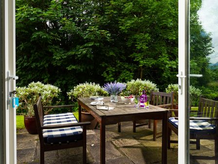 An outdoor patio with a wooden table and chairs with blue and white cushions and plants in pots at Tethera in Keswick