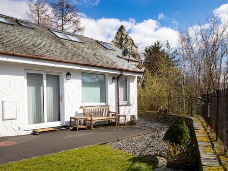 An exterior view of a white house with wooden bench and table on the patio near a garden and trees at Lingmoor View in Chapel Stile