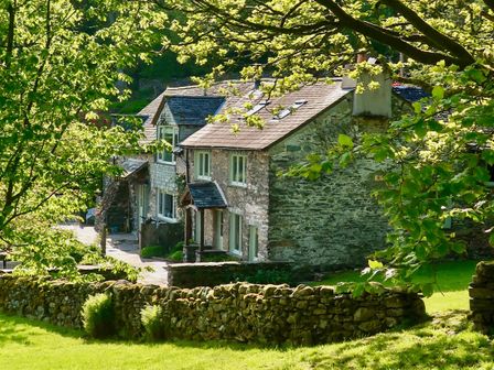 A stone house with multiple windows behind a stone wall and surrounded by trees at High Cunsey Farm in Far Sawrey