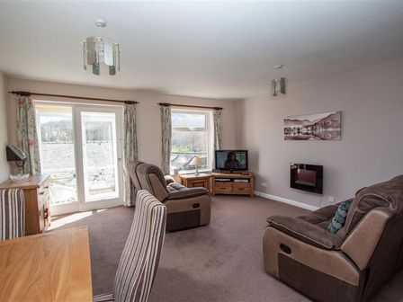 A living room with brown recliner chairs a wooden TV stand a mounted electric fireplace and floral curtains at Mellbreak in Chapel Stile