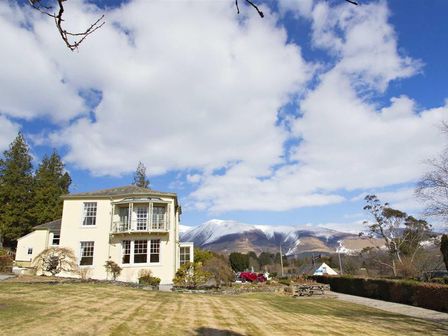 A two story house with a lawn and snow capped mountains in the background at Derwentwater House in Portinscale