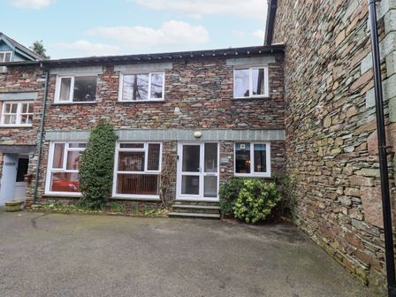 A stone building with white framed windows and a glass door with plants in front at Molly's Cottage in Grasmere