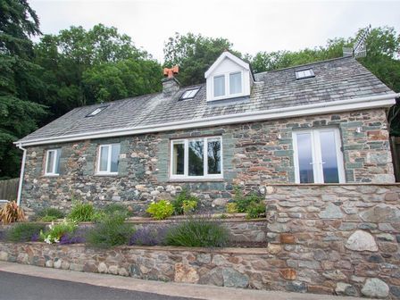 Exterior view of a stone cottage with multiple windows and a stone garden wall at Dancing Beck Cottage in Millbeck