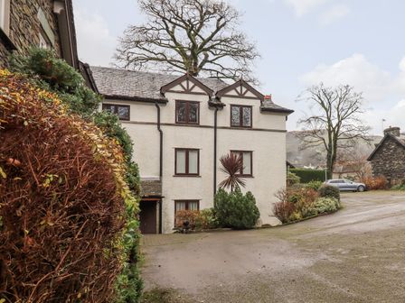 A driveway leading to a white multi-story house with brown windows surrounded by bushes and trees at Loughrigg View in Ambleside