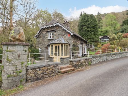 A stone cottage with a small porch and a stone wall along a road at North Lodge in Grasmere