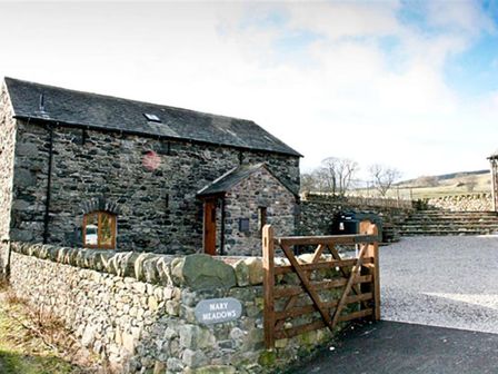 Stone building with slate roof behind wooden gate and stone wall at Mary Meadows Barn in Dockray