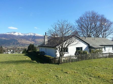 A house with a fenced yard and trees with snow-capped mountains in the background at Bandol in Braithwaite
