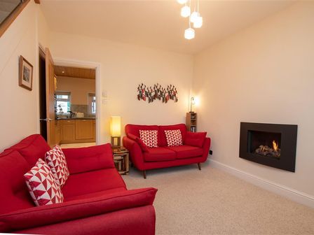 A living room with red sofas a wall-mounted fireplace and a door opening to a kitchen at Gable End in Braithwaite
