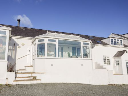A white building with a glass conservatory and steps leading up to it at 5 Porthdafarch South Cottages in Porthdafarch near Trearddur Bay