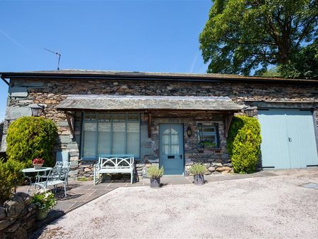 A stone building with a blue door and large window with outdoor seating and plants at The Coach House Ambleside
