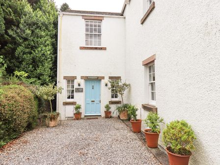 The exterior of a white house with a blue door and several potted plants on a gravel driveway at Grisedale View Keswick