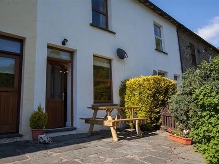 An outdoor patio area with a wooden picnic table potted plants and shrubs outside a white building at Robins Nest in Coniston