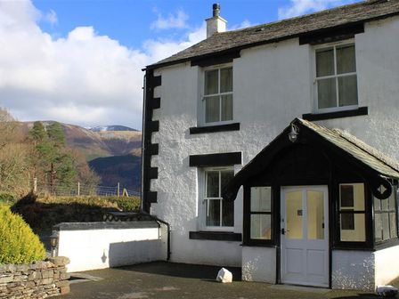 Exterior view of a white house with black trim surrounded by trees and hills at Pen Cottage in Thornthwaite