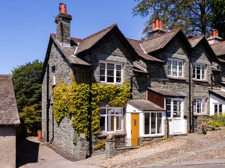 Stone house with multiple chimneys and windows with climbing plants on the walls at Rock Lea Ambleside