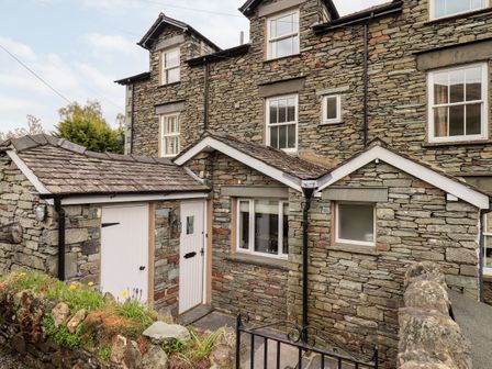 A stone house with white doors and windows and a small garden in front at Holmdale in Grasmere