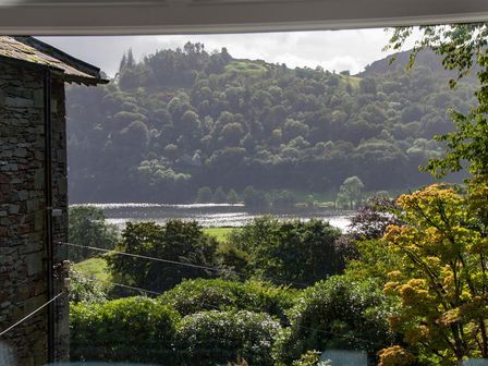 A view of a lake surrounded by trees and hills with a stone building on the left at Helm Crag in Grasmere