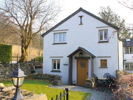 A white house with a wooden door and outdoor table set in a garden at Forest Cottage in Coniston