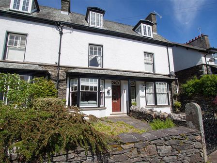 A white two-story house with a stone wall and garden in front at Greystones in Bowness