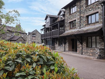 Stone buildings along a paved road with green shrubs in front at Jenever Cottage in Ambleside
