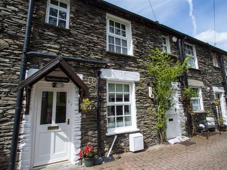 An exterior view of a stone house with white framed windows and doors with plants outside at Swallow's Nest in Windermere