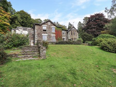A stone house with multiple windows surrounded by grass and trees at Easedale in Grasmere