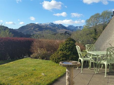 A garden with green metal chairs and table on a patio and mountains in the background at Rothay 18 in Ambleside