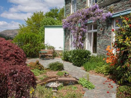 A garden with a stone path a wooden bench a small pond and purple flowers on a building at Betamere in Ambleside
