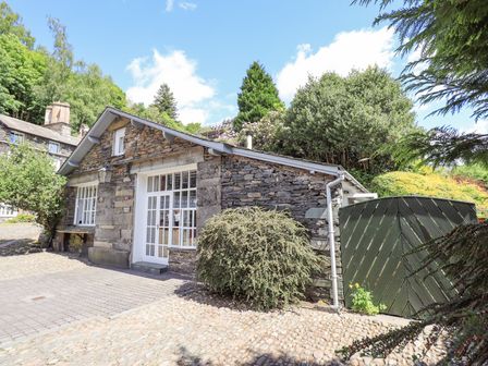 A stone cottage with white windows and door surrounded by greenery and paved ground at Courtyard Cottage in Ambleside