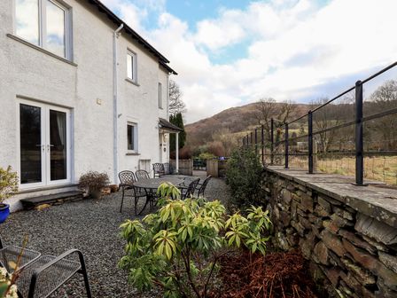 An outdoor patio with metal chairs and tables next to a white building and a stone wall with a hill in the background at Wansfell Ambleside