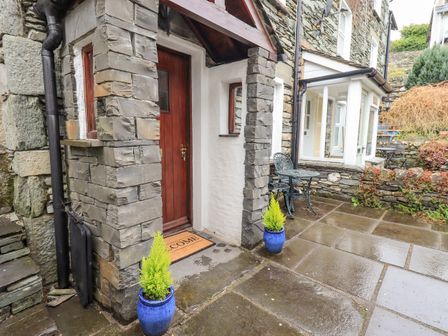 Stone house entrance with wooden door two blue pots with plants and metal table and chairs on wet stone patio at Hideaway Cottage Ambleside