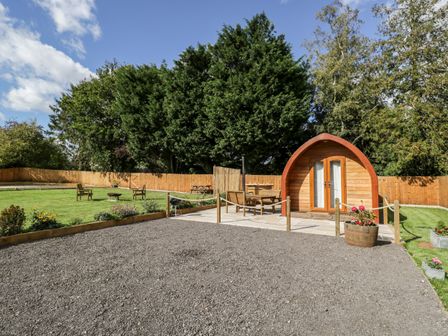 A garden area with a wooden pod seating and chairs on patio with trees and fence at Halmore Pod Halmore near Berkeley