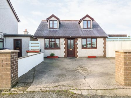 A detached house with two dormer windows a paved driveway and brick pillars at Rhiangwyn Cottage in Llanrhyddlad near Cemaes Bay