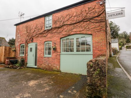 A brick house with green doors and windows and a sign saying Ostlers in Mitcheldean