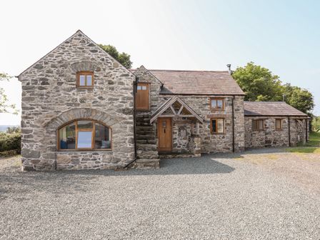 A stone house with wooden windows and doors with a gravel driveway at Ty Cerrig in Llanddaniel near Llanfairpwllgwyngyll