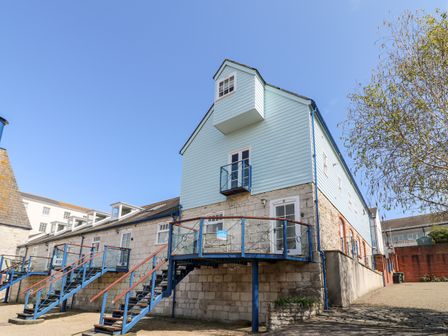 A stone and blue wooden building with external staircases and balconies under a clear sky at Santiago House in Weymouth