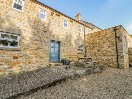 A stone exterior wall of a house with windows a blue door a picnic table and a dog on a gravel surface at Todridge Barn in Corbridge