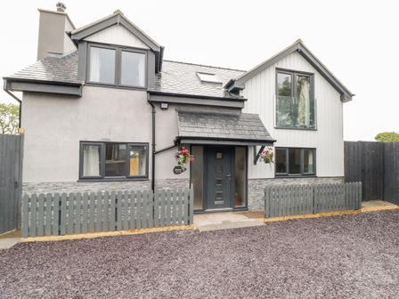 The exterior of a modern two-story house with a grey fence and gravel driveway at Hunters Cottage in Tyn-y-Gongl near Benllech
