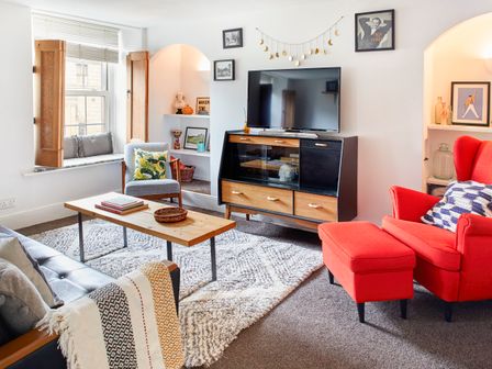 A living room with a red armchair a wooden coffee table and a television on a wooden stand at 1 Pringles Yard in Alnwick